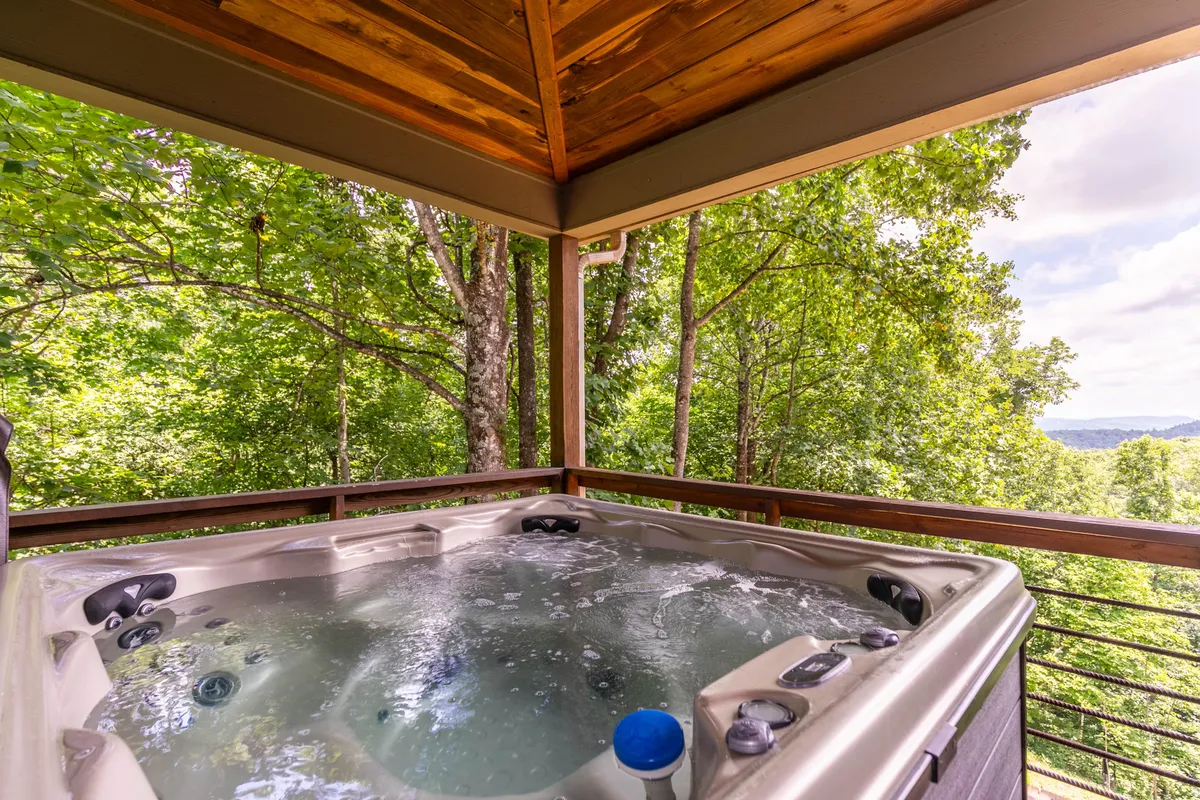 An inviting hot tub on an outdoor deck, surrounded by greenery with a sweeping view of distant hills. The setup encourages family relaxation and taking in the natural beauty after a day of adventure.