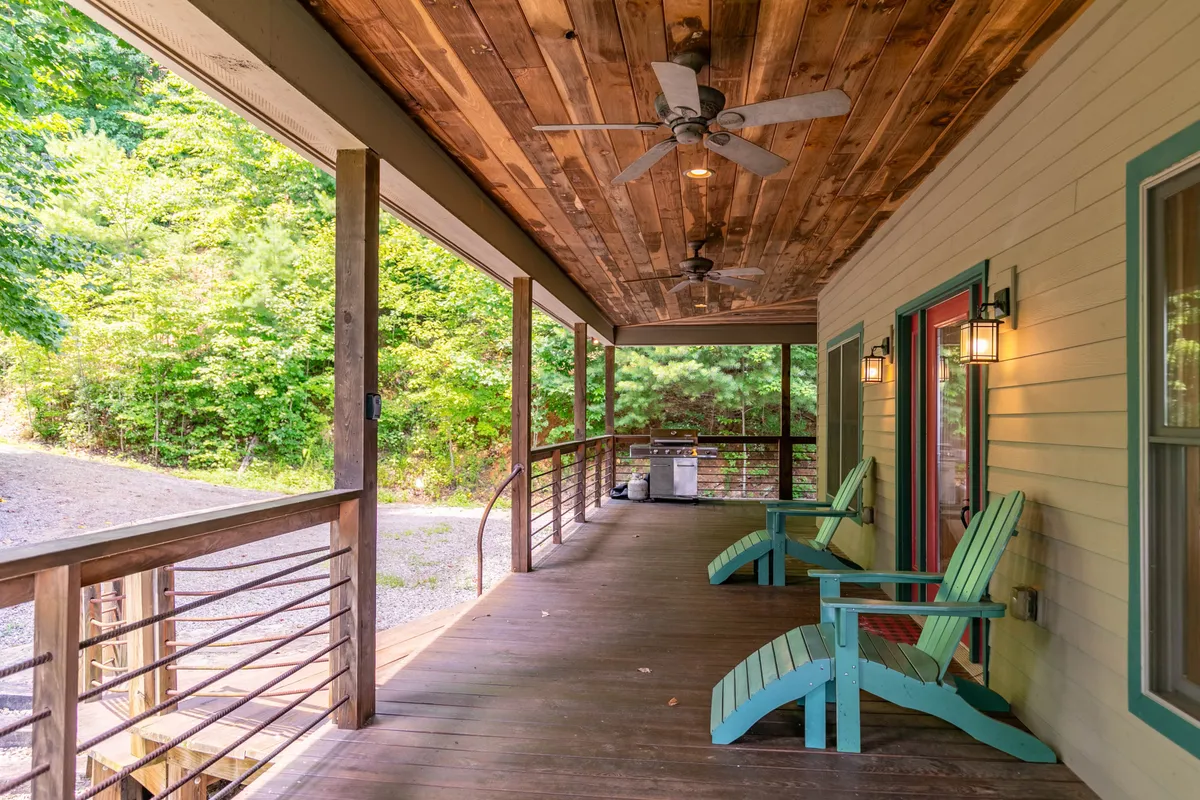 This photo highlights a peaceful exterior deck with Adirondack chairs, wooden railings, exterior lights, and a wooden ceiling, all set against a calm, tree-filled backdrop. The space is perfect for morning coffee, sunset viewing, or simply relaxing with your furry companions.