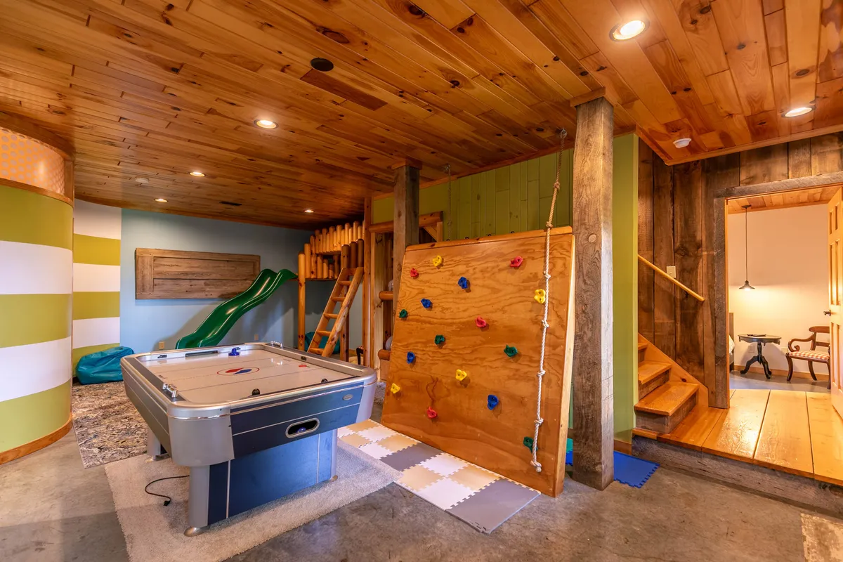 This image captures the heart of the Adventure & Play Family Zone with its vibrant play area. Visible are the air hockey table, rock climbing wall, and a bright green slide attached to the built-in bunk beds. Wooden stairs and playful accents add to the sense of fun and adventure, inviting children to climb, play, and slide.