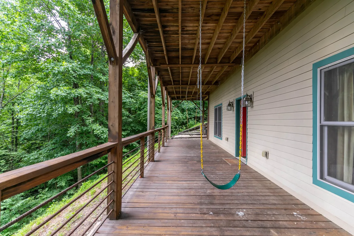 A cozy porch with a wooden swing, railings, and views of lush greenery in the background. The swing invites guests to relax, read, or share stories with loved ones while enjoying the fresh mountain air.