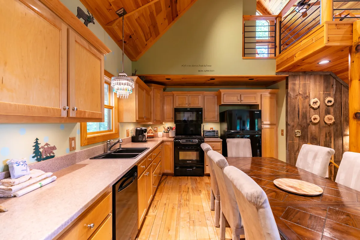 A view of the kitchen and adjacent dining area, featuring a large, expandable table, a kitchen island, and warm wooden cabinetry under an elegant chandelier. The scene radiates warmth and invites communal cooking, dining, and conversation.