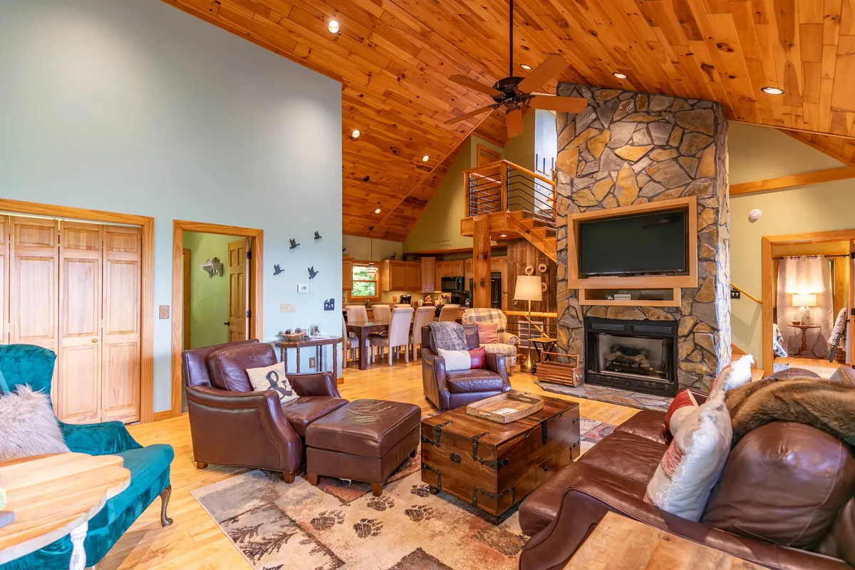An open-concept living and dining space featuring a stone fireplace, vaulted wooden ceiling, and a comfortable seating area ideal for family gatherings. The dining table sits nearby, blending seamlessly with the living area, and is well-positioned for shared meals or evening games.