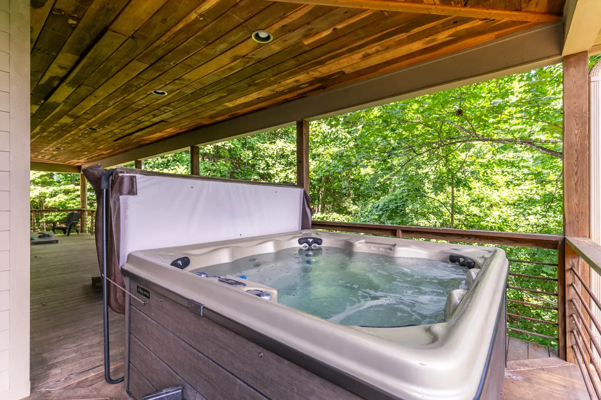 A hot tub set on a wooden deck is enveloped by greenery, providing privacy amidst nature. The scene invites guests to relax and rejuvenate, whether after outdoor adventures or while socializing with loved ones. The deck’s position underscores the cabin’s immersive mountain setting.